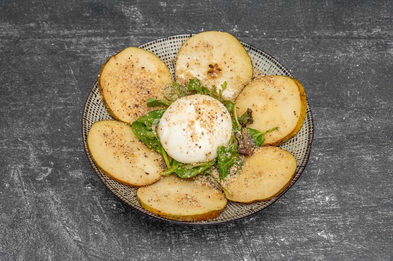 Assiette de tranches de pommes de terre rôties entourant une burrata, servie sur un lit de roquette et assaisonnée.