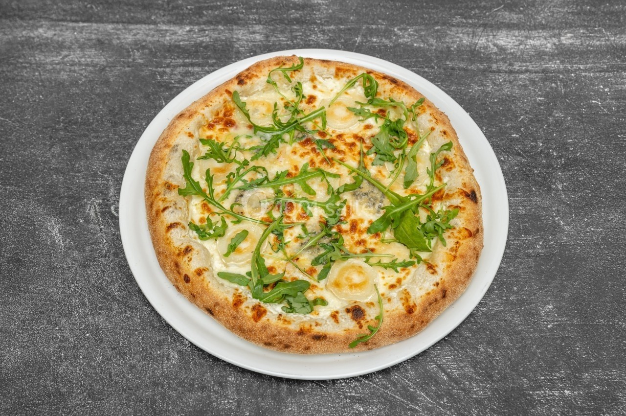 Pizza garnie de fromage, roquette et sauce blanche, servie sur une assiette blanche sur une table grise.