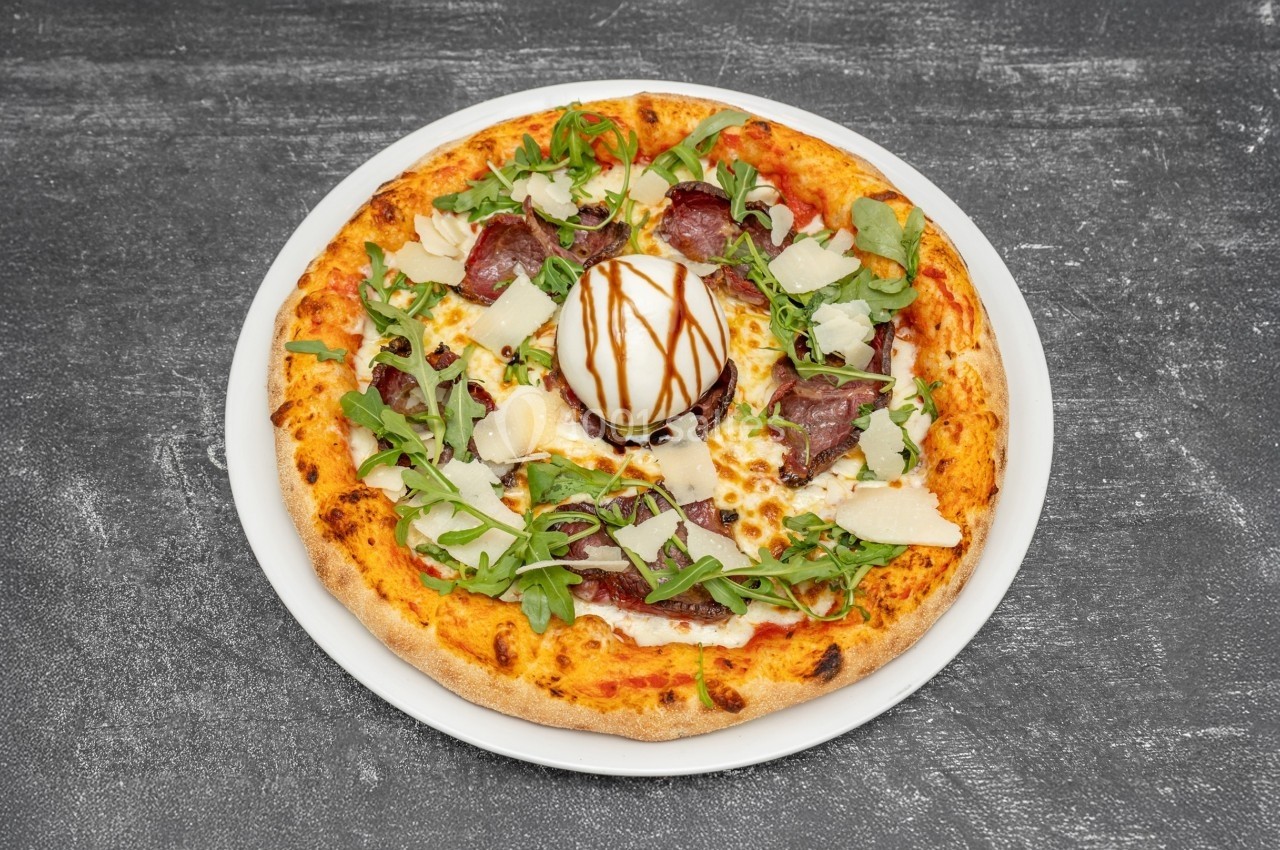 Pizza garnie de roquette, charcuterie, copeaux de fromage, burrata et filet de vinaigre balsamique.