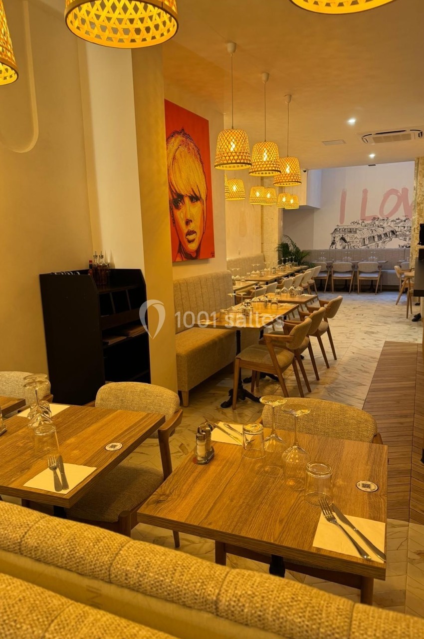 Salle de restaurant chaleureuse avec tables en bois, chaises rembourrées, éclairage suspendu et décoration murale colorée.