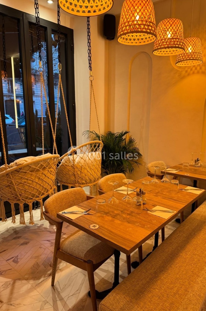 Salle de restaurant chaleureuse avec table en bois, chaises, banquette, balançoires suspendues et éclairage tamisé.