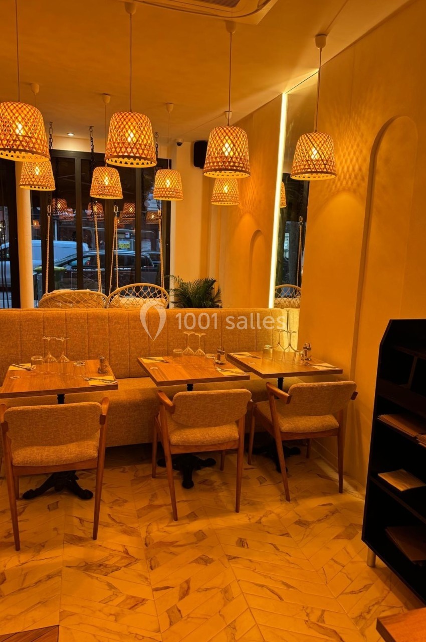 Salle de restaurant chaleureuse avec tables en bois, chaises rembourrées et suspensions lumineuses en osier.