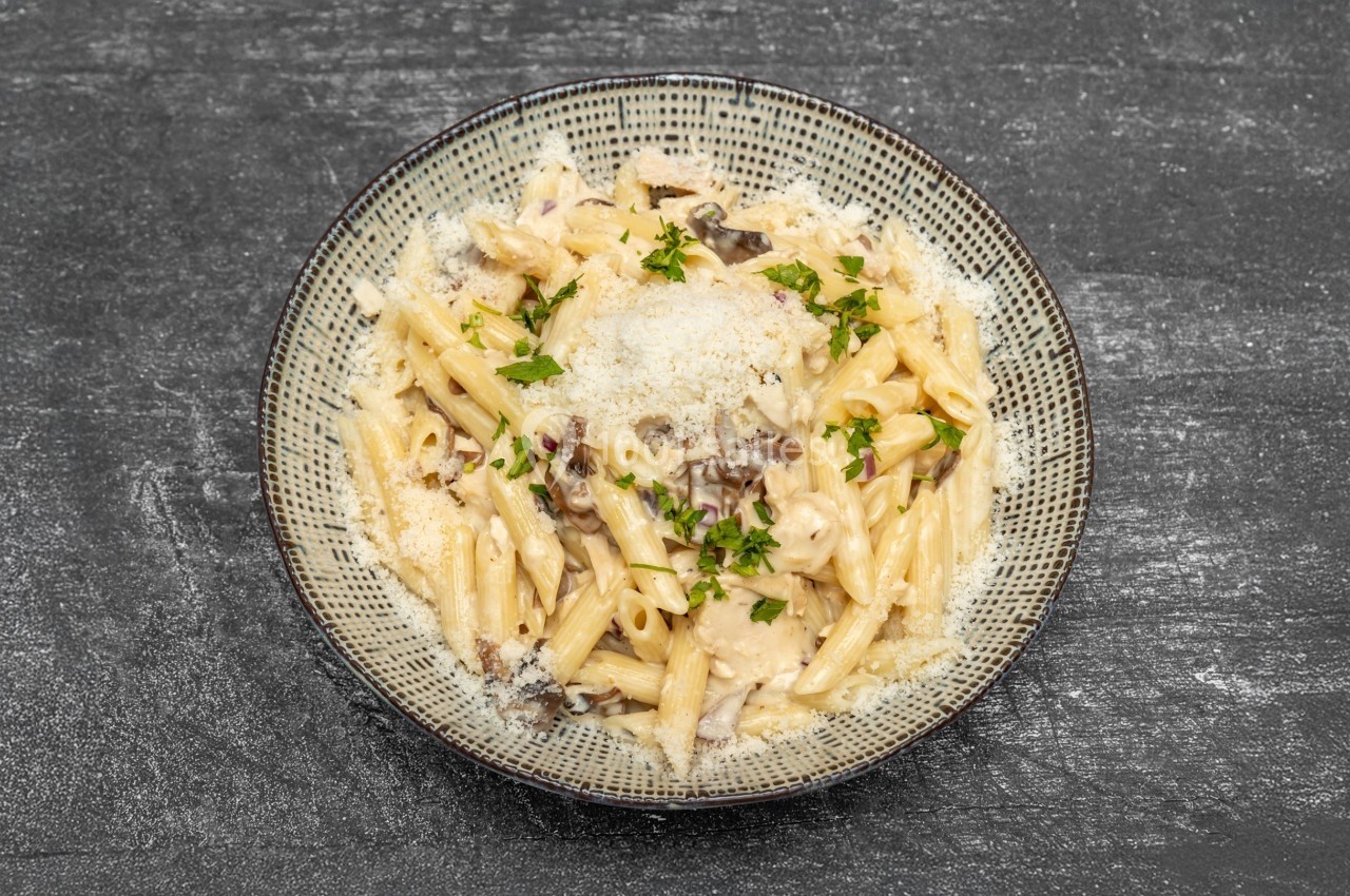 Assiette de pâtes crémeuses garnies de persil frais et de fromage râpé, servie sur une table sombre.