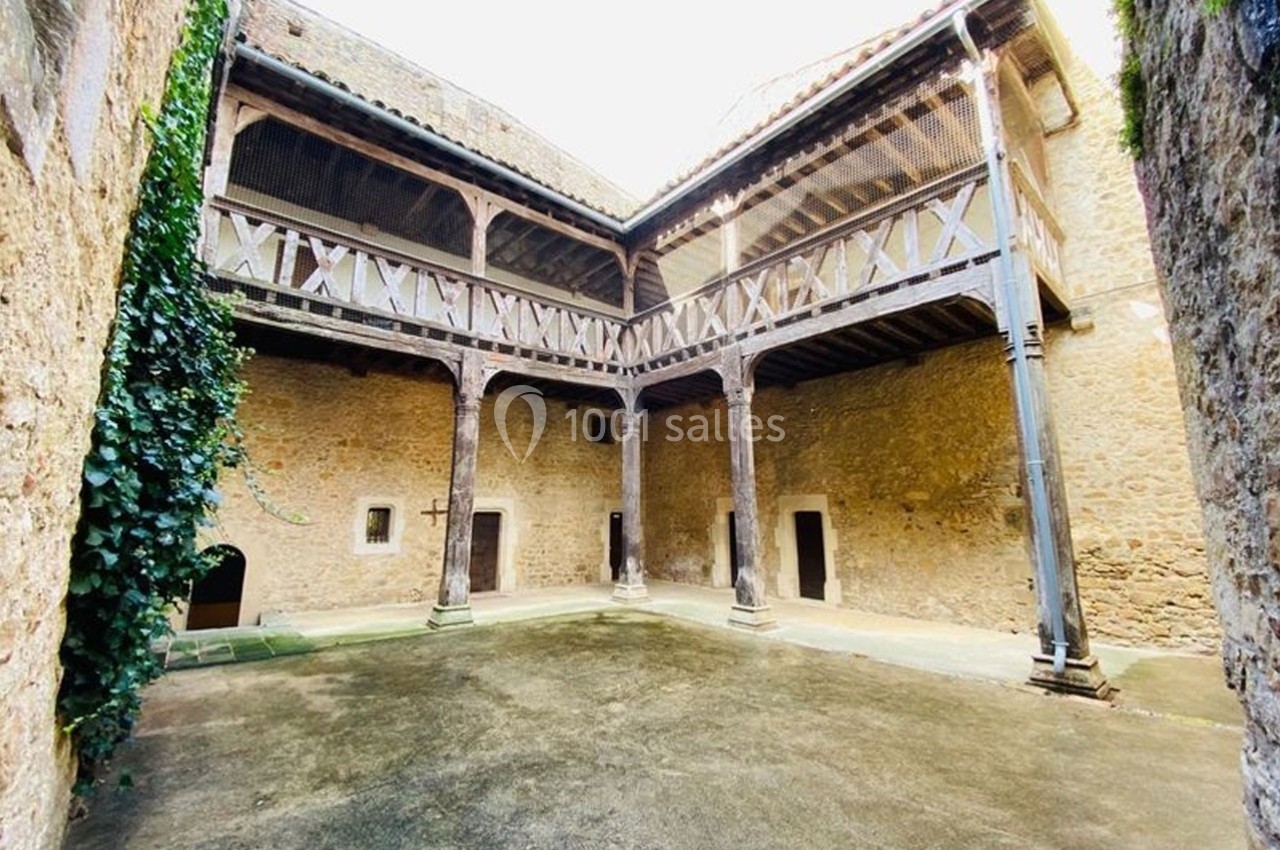 Cour intérieure en pierre avec galerie en bois à l'étage, entourée de murs anciens et partiellement couverte de végétation.