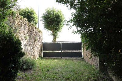 Miniature Location salle Saint-Félix-Lauragais (Haute-Garonne) - La Commanderie #10 Portail métallique noir fermé entre deux murs en pierre, entouré de végétation et d'arbustes.