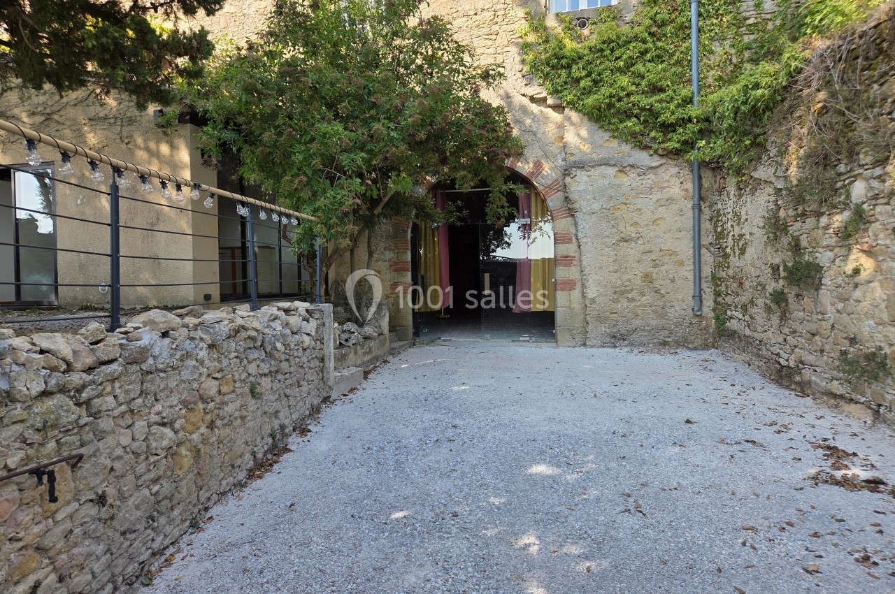 Entrée d'un bâtiment en pierre avec une arche, entourée de végétation et d'un sol en gravier.