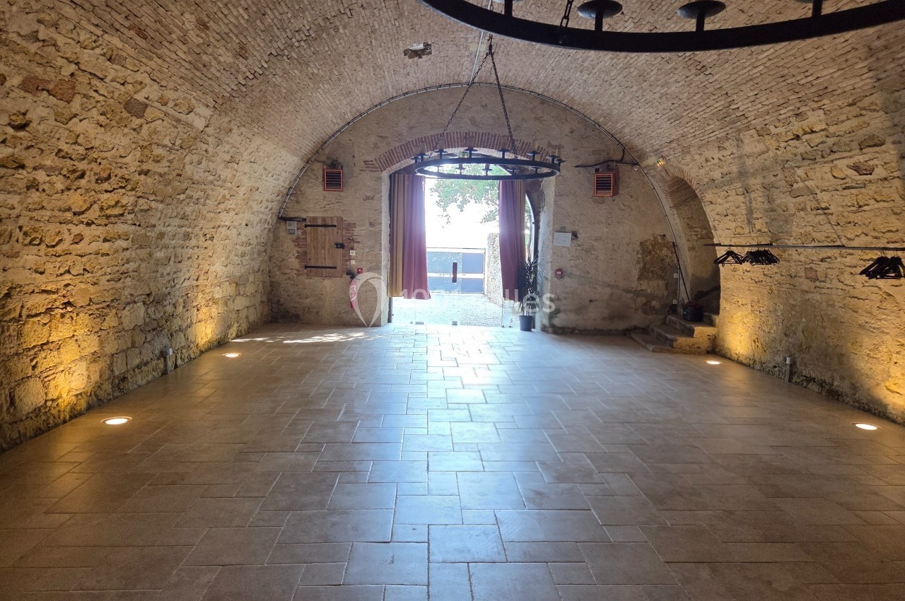 Salle voûtée en pierre avec un sol carrelé, éclairage tamisé et vue sur une ouverture donnant sur l'extérieur.