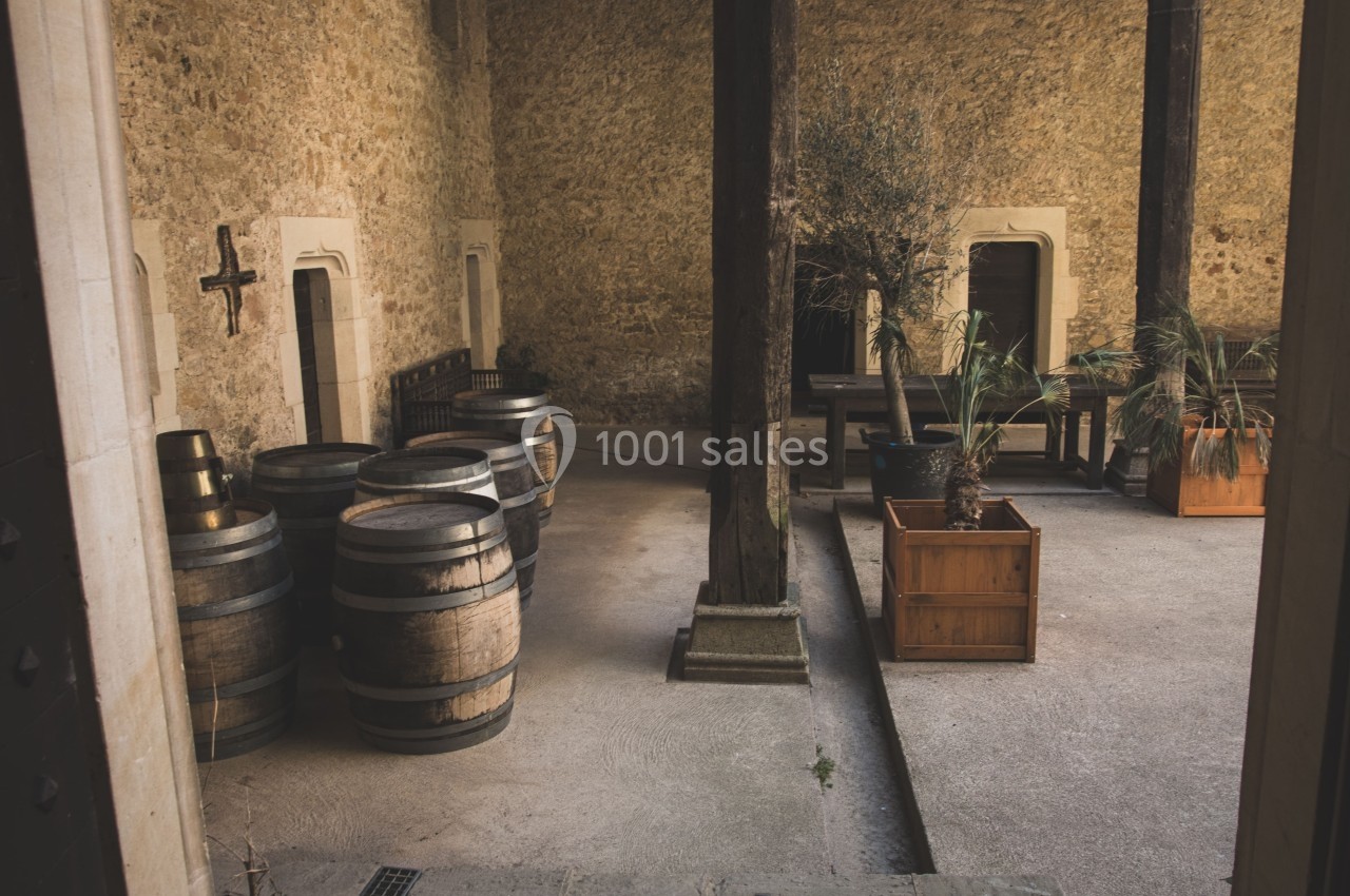 Cour intérieure avec murs en pierre, tonneaux en bois, plantes en pot et mobilier rustique.
