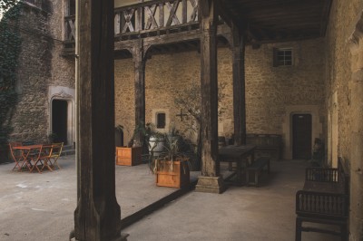 Miniature Location salle Saint-Félix-Lauragais (Haute-Garonne) - La Commanderie #7 Salon rustique avec murs en pierre, canapés en cuir, tapis ancien et lumière naturelle entrant par une porte ouverte.