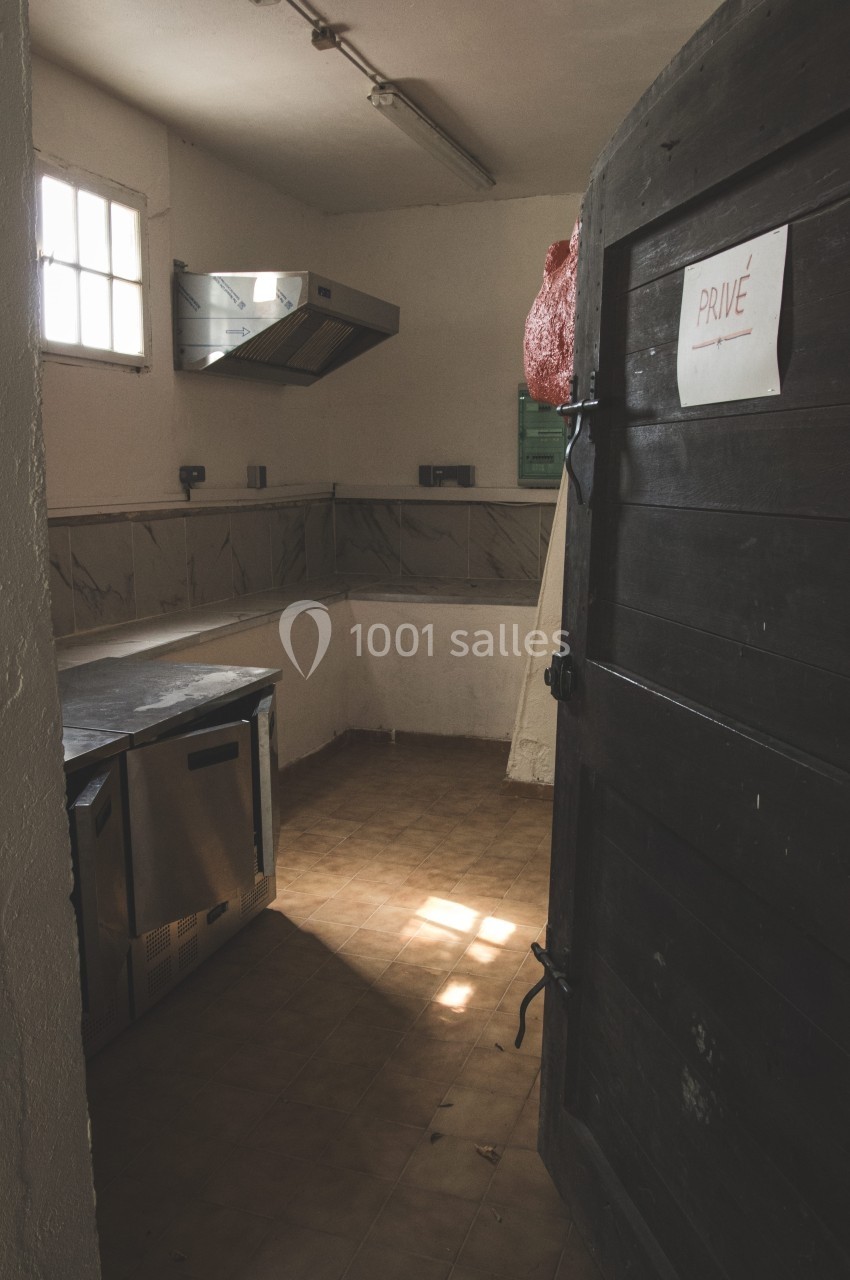 Cuisine vide avec plan de travail en inox, hotte murale, sol en carrelage beige et porte en bois portant un panneau ’Privé’.