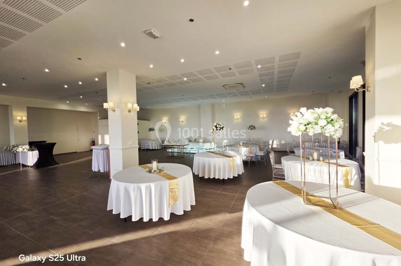 Salle de réception lumineuse avec tables rondes décorées de nappes blanches et centres de table floraux.