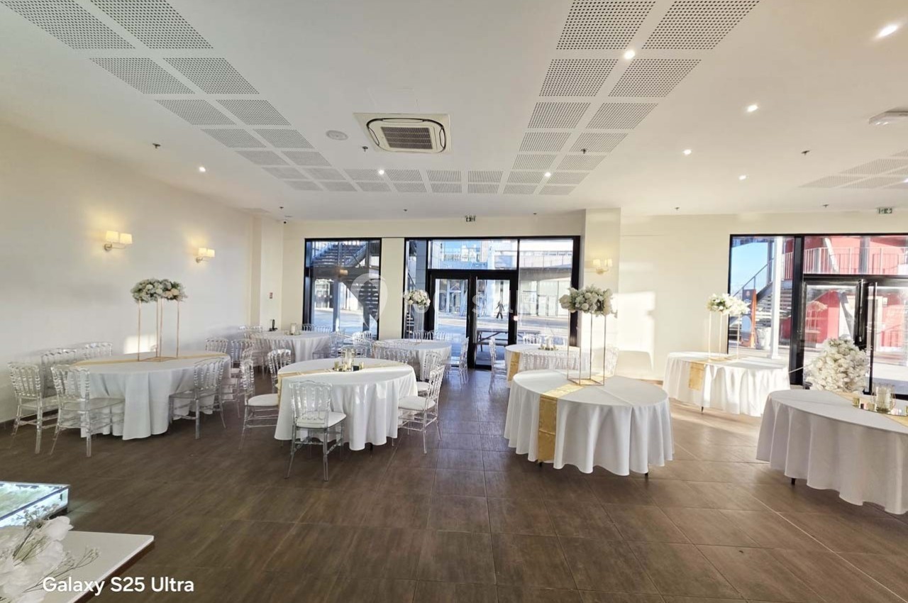 Salle de réception lumineuse avec tables rondes et rectangulaires décorées de nappes blanches et centres de table fleuris.