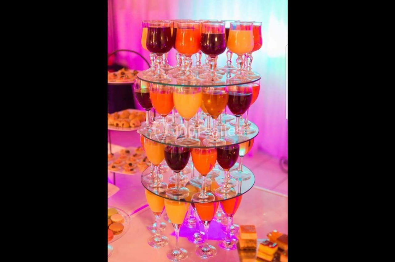 Présentoir à plusieurs étages avec des verres de cocktails colorés, entouré d'un décor lumineux et festif.