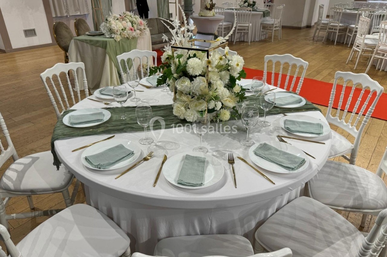 Table ronde élégamment dressée avec nappes blanches, serviettes vertes, couverts dorés et centre de table floral.
