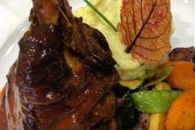 Assiette contenant un morceau de viande avec sauce, légumes rôtis, chips croustillante et garniture verte.