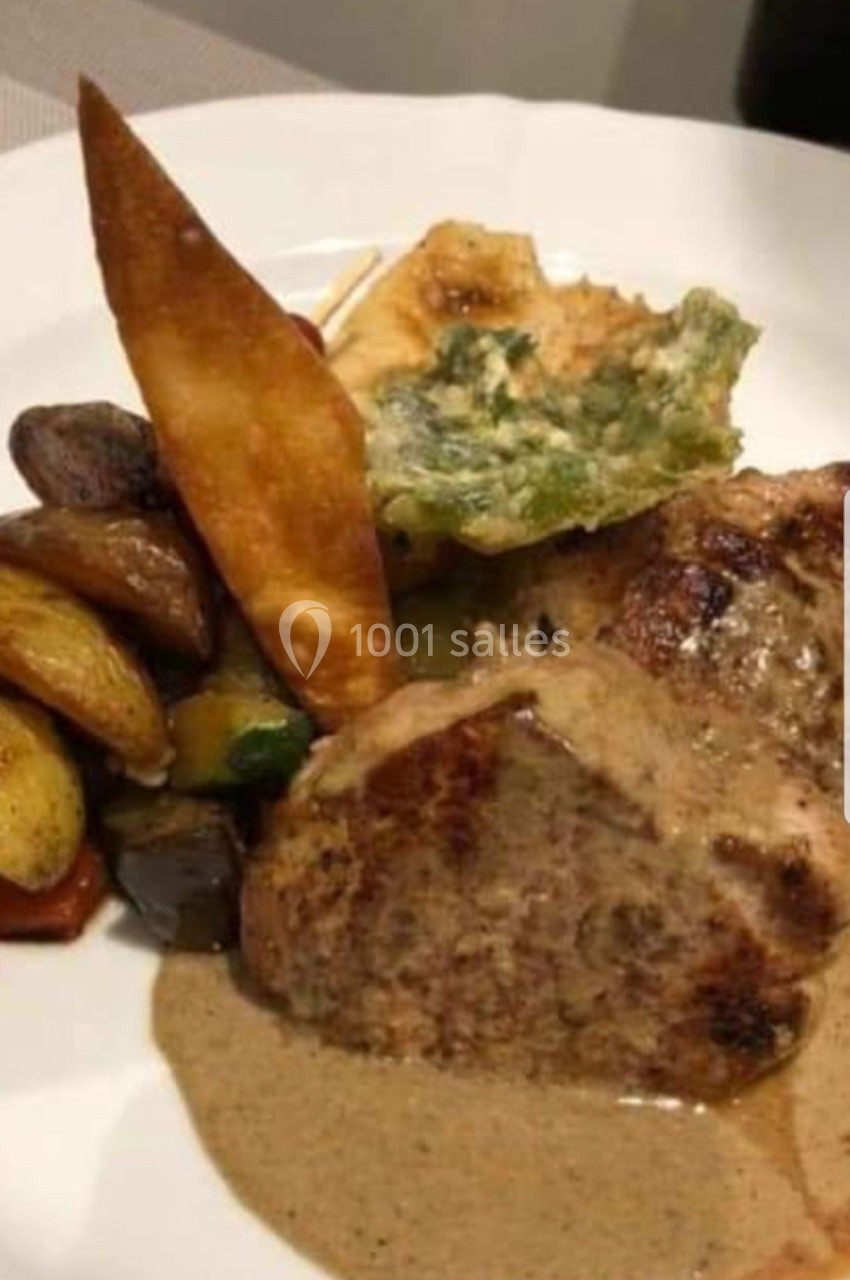 Assiette contenant un morceau de viande avec sauce, légumes rôtis, chips croustillante et garniture verte.