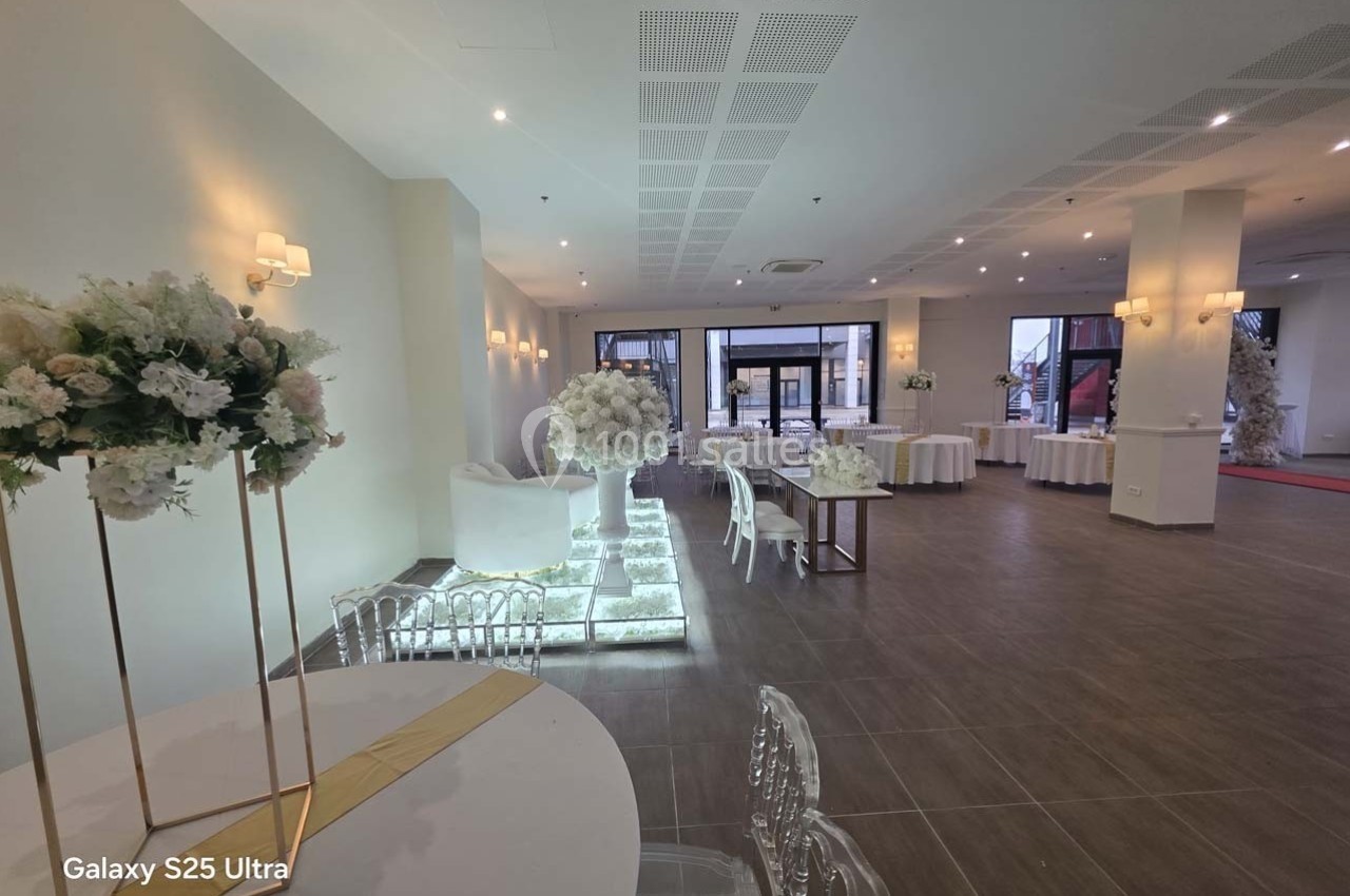 Salle de réception élégante avec tables décorées de fleurs blanches, éclairage doux et grandes baies vitrées.