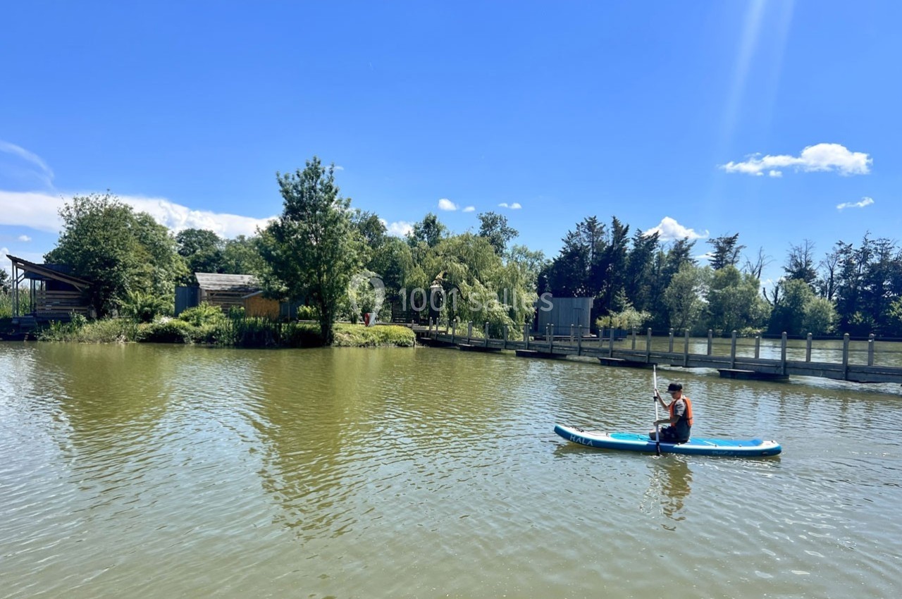 Une personne fait du paddle sur un lac entouré de verdure par une journée ensoleillée.