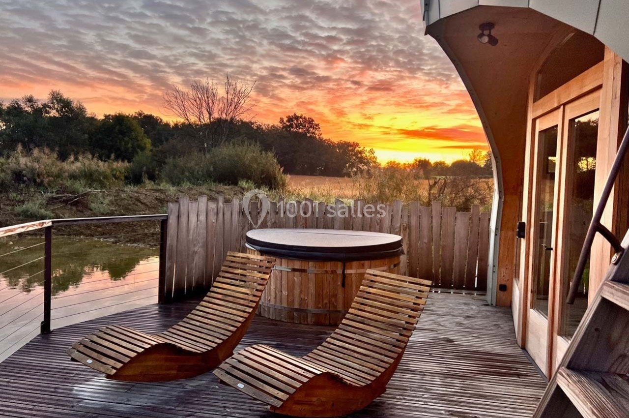 Terrasse en bois avec deux chaises longues et un bain nordique, offrant une vue sur un coucher de soleil et un paysage…