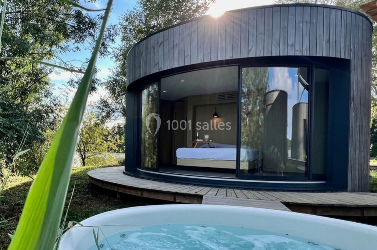 Cabane moderne en bois avec grande baie vitrée donnant sur un jacuzzi extérieur entouré de verdure.