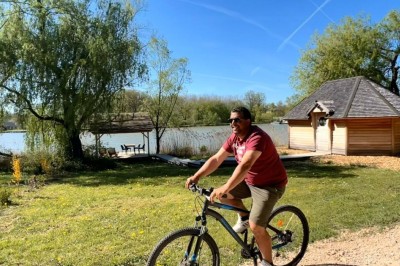 Un panier en osier et des produits alimentaires sont disposés sur une table en bois près d'un étang entouré de végétation.