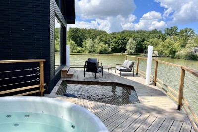 Intérieur d'une cabane en bois avec table ronde, chaises métalliques, canapé et terrasse extérieure visible.