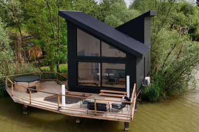 Intérieur d'une cabane en bois avec table ronde, chaises métalliques, canapé et terrasse extérieure visible.