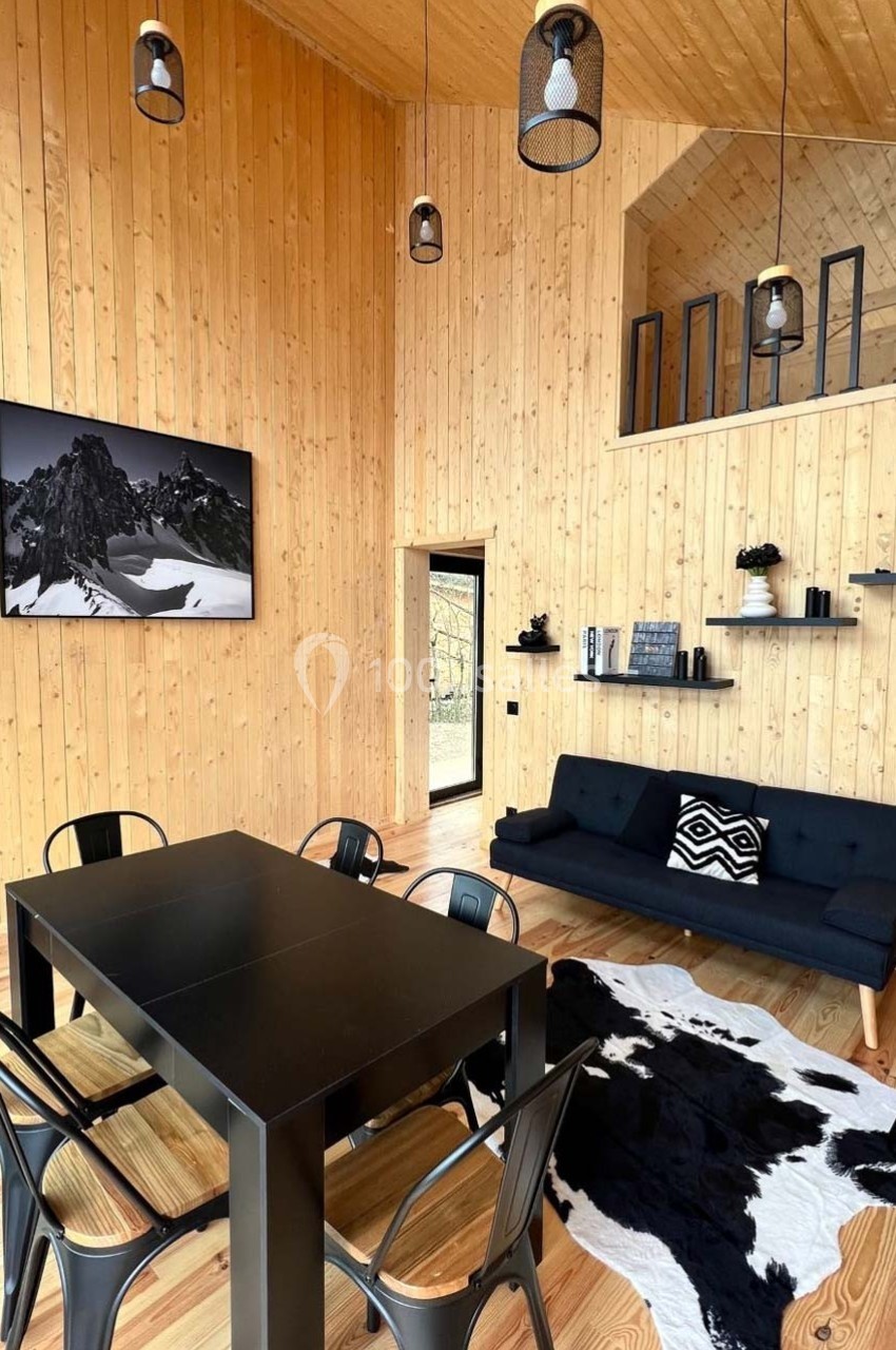 Salle à manger et salon avec murs en bois, table noire, chaises métalliques, canapé, tapis en peau et décoration moderne.
