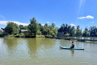 Intérieur d'une cabane en bois avec table ronde, chaises métalliques, canapé et terrasse extérieure visible.