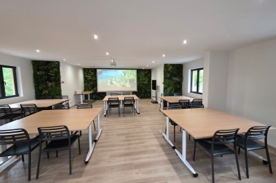 Intérieur d'une cabane en bois avec table ronde, chaises métalliques, canapé et terrasse extérieure visible.
