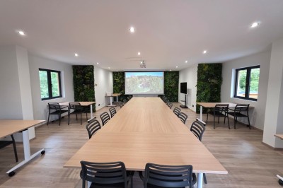 Intérieur d'une cabane en bois avec table ronde, chaises métalliques, canapé et terrasse extérieure visible.