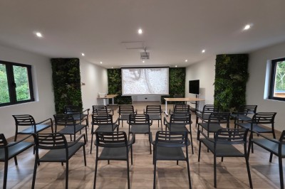 Intérieur d'une cabane en bois avec table ronde, chaises métalliques, canapé et terrasse extérieure visible.