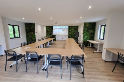Intérieur d'une cabane en bois avec table ronde, chaises métalliques, canapé et terrasse extérieure visible.
