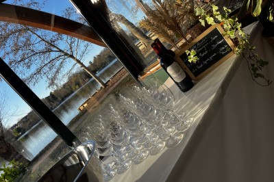 Table dressée avec une nappe blanche, couverts, verres, centre de table floral et vue sur un paysage extérieur verdoyant.
