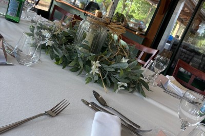 Table dressée avec une nappe blanche, couverts, verres, centre de table floral et vue sur un paysage extérieur verdoyant.