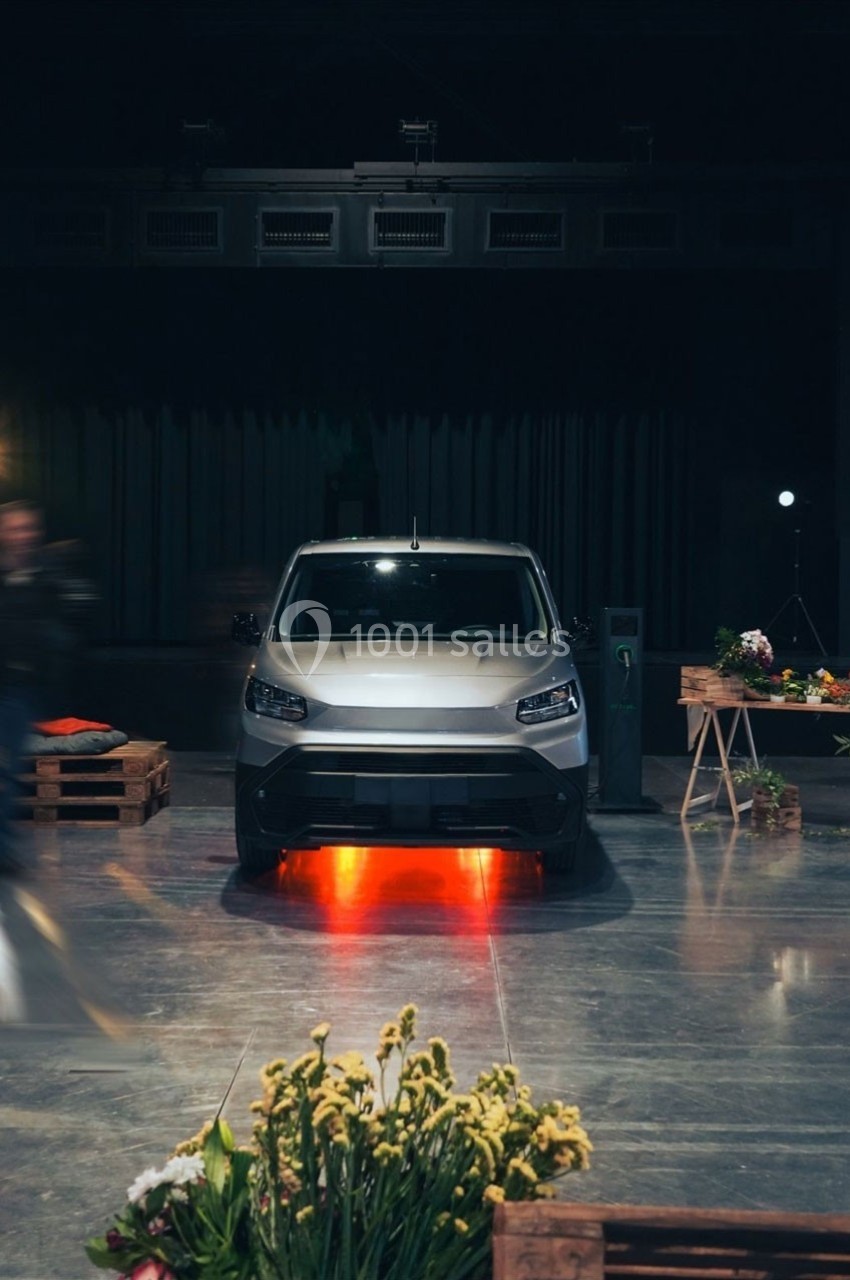 Un véhicule électrique gris exposé dans un espace intérieur, éclairé par des lumières rouges sous le châssis.