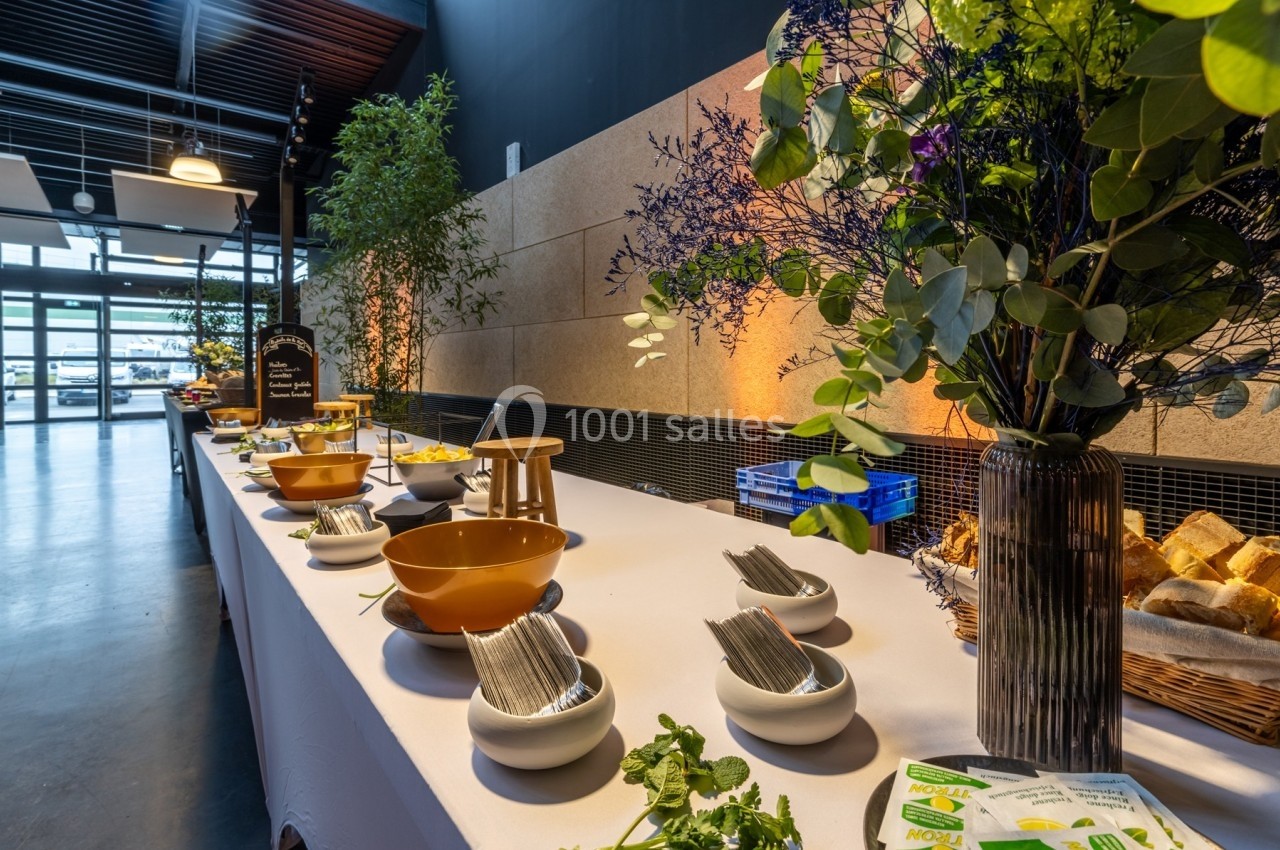 Buffet avec bols, couverts, pains et décorations florales sur une table blanche dans une salle lumineuse.