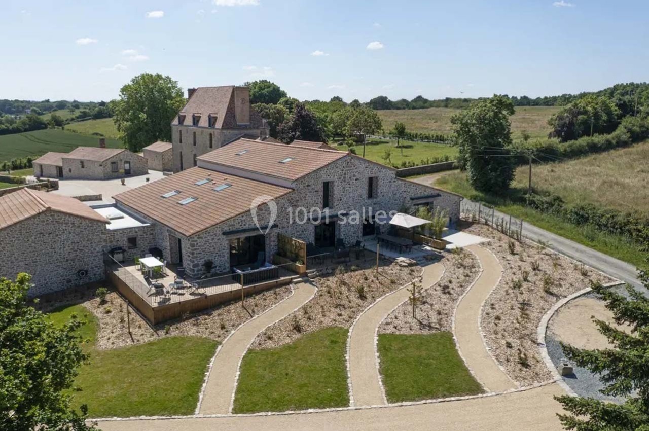 Vue aérienne d'un bâtiment en pierre rénové avec toits en tuiles, entouré de chemins et de verdure en milieu rural.