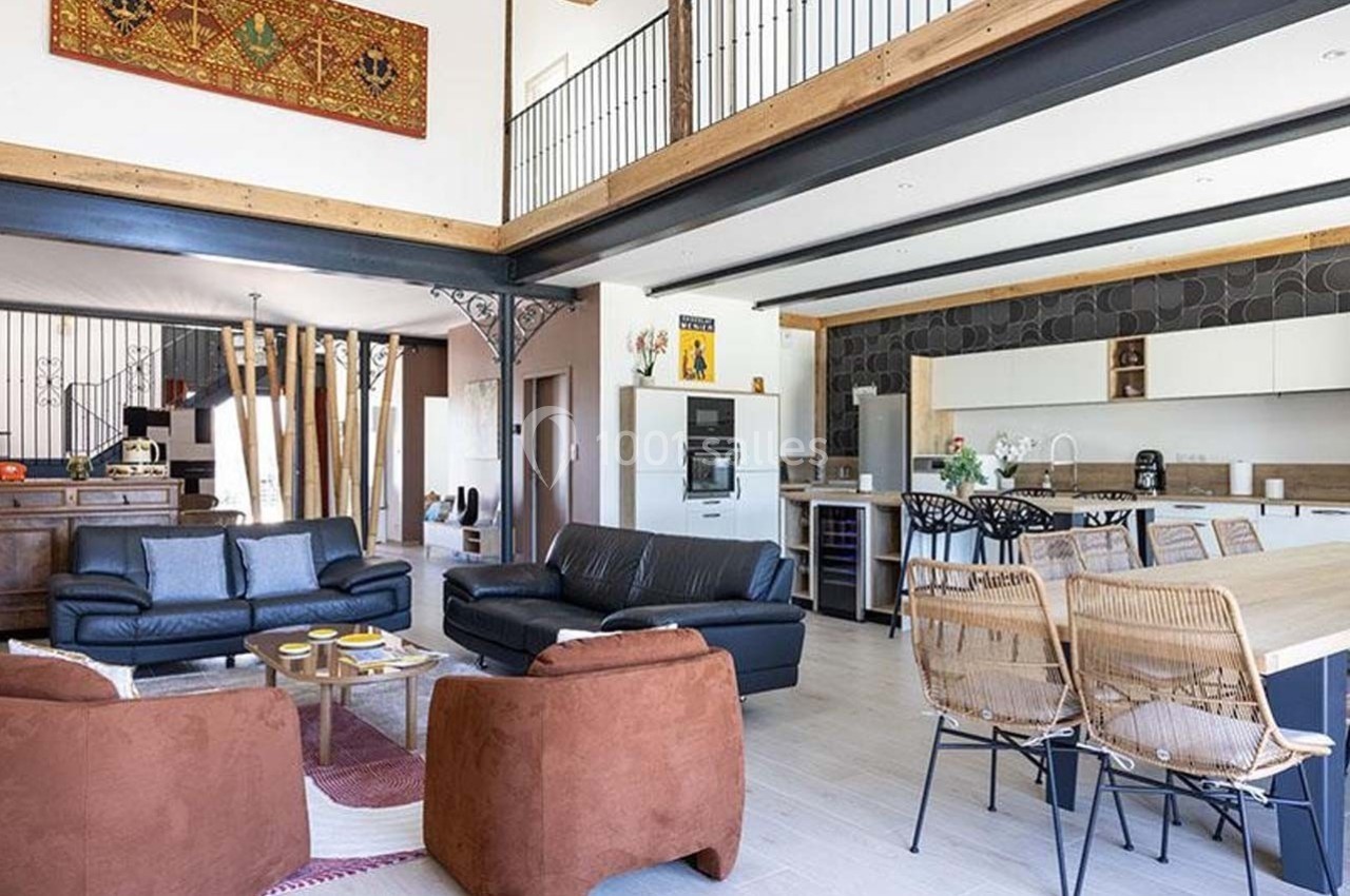 Salon spacieux avec canapés, table basse, cuisine ouverte moderne et mezzanine en bois.