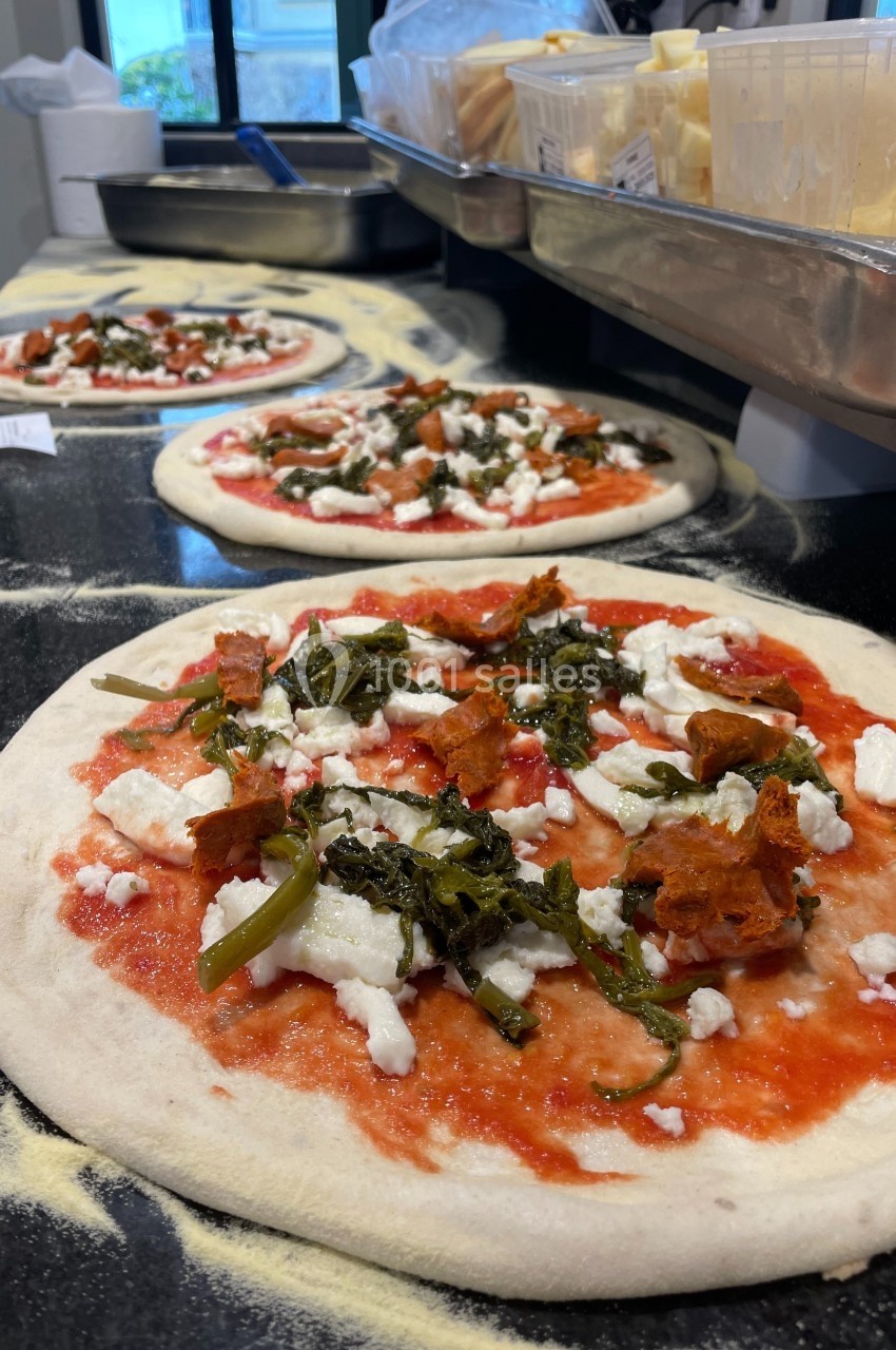 Pizzas crues garnies de sauce tomate, fromage, légumes verts et morceaux de viande, prêtes à être enfournées.