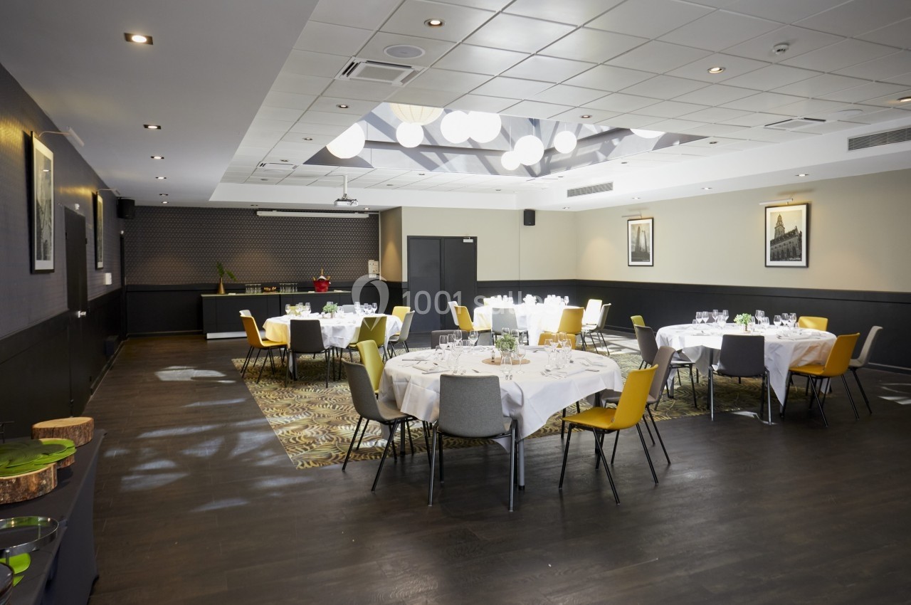 Salle de réception lumineuse avec tables rondes dressées, chaises jaunes et grises, et décor moderne.