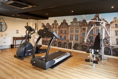 Feuilles vertes dans un vase doré sur une étagère près d'une fenêtre donnant sur une rue urbaine avec bâtiments et grue.