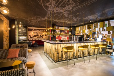 Feuilles vertes dans un vase doré sur une étagère près d'une fenêtre donnant sur une rue urbaine avec bâtiments et grue.