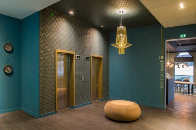 Feuilles vertes dans un vase doré sur une étagère près d'une fenêtre donnant sur une rue urbaine avec bâtiments et grue.