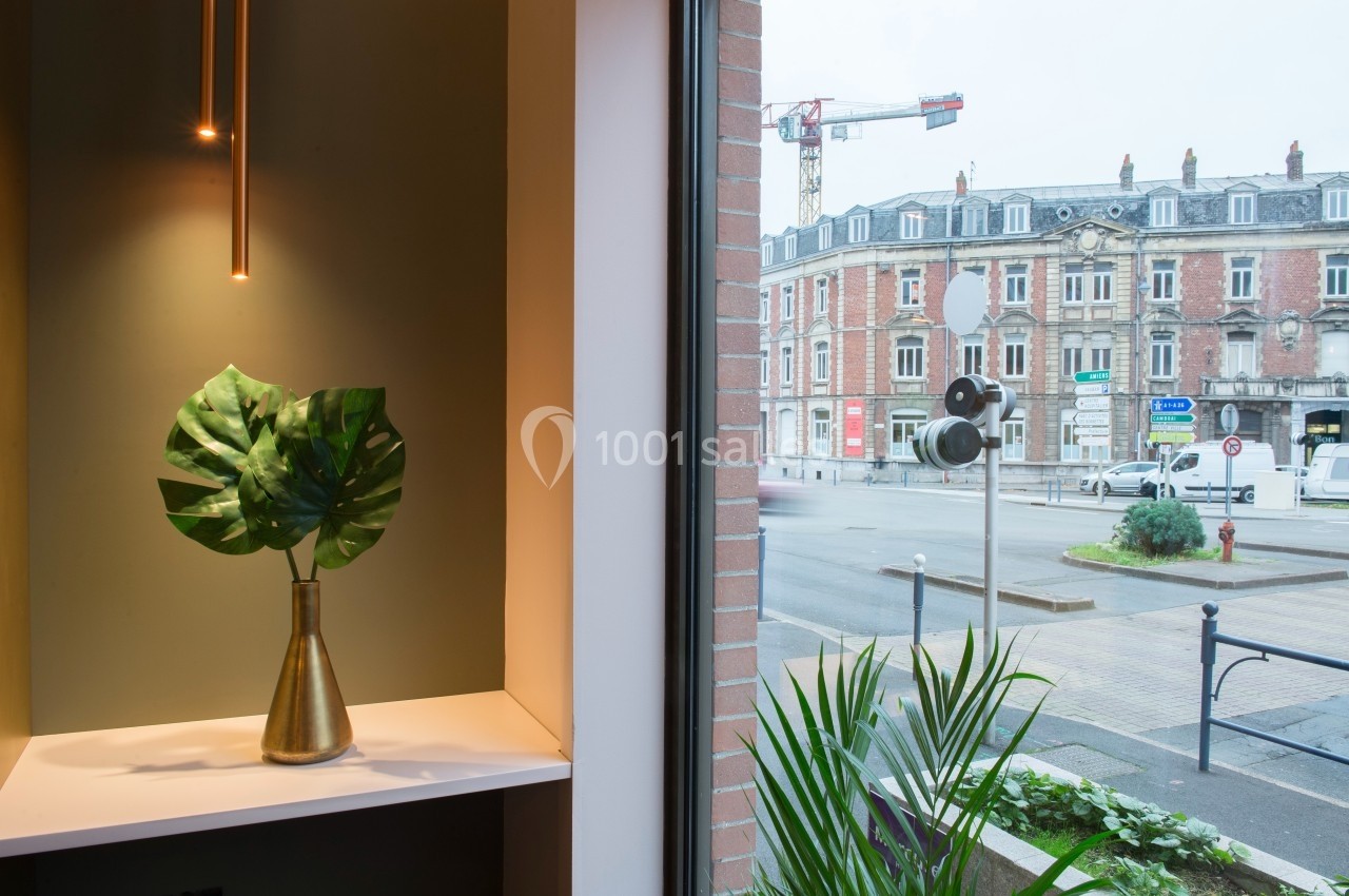 Feuilles vertes dans un vase doré sur une étagère près d'une fenêtre donnant sur une rue urbaine avec bâtiments et grue.