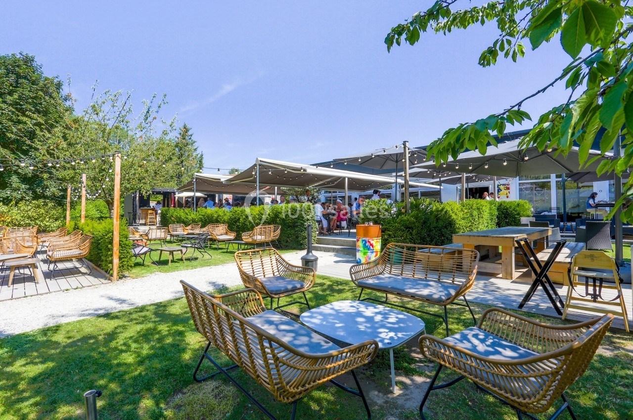 Terrasse extérieure avec mobilier en rotin, tables basses, parasols et verdure sous un ciel dégagé.