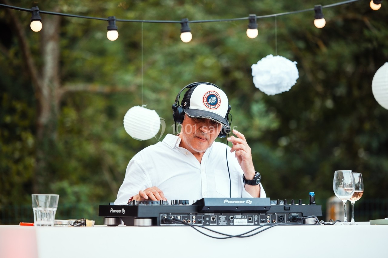 Un DJ mixe en plein air sous des guirlandes lumineuses, entouré de décorations blanches suspendues.