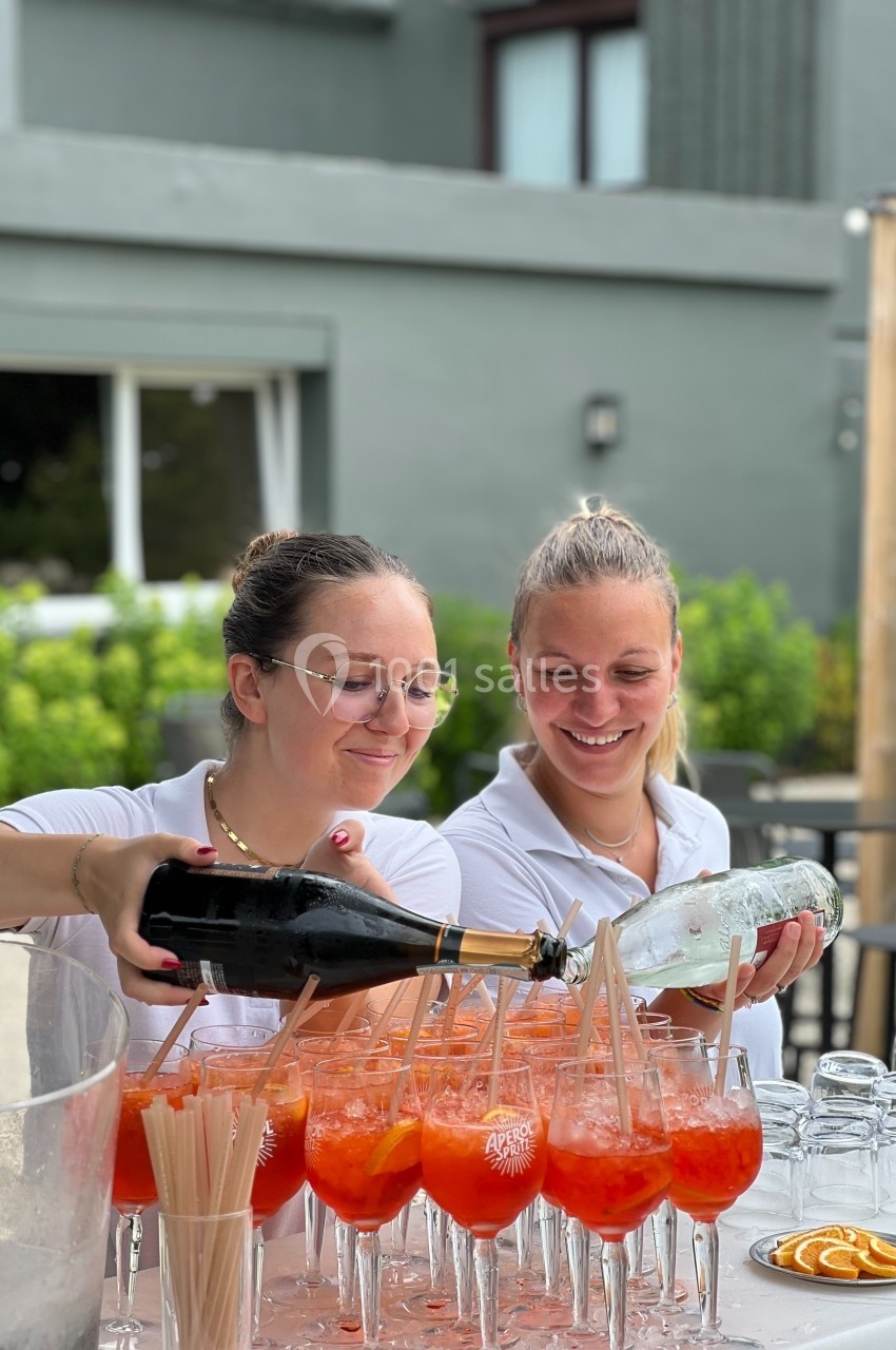 Deux femmes préparent des cocktails orange avec des tranches d'agrumes sur une table en extérieur.