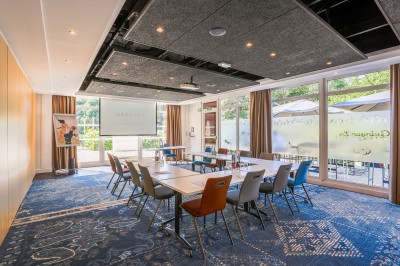 Salle de conférence avec des rangées de chaises colorées face à un écran de projection allumé.