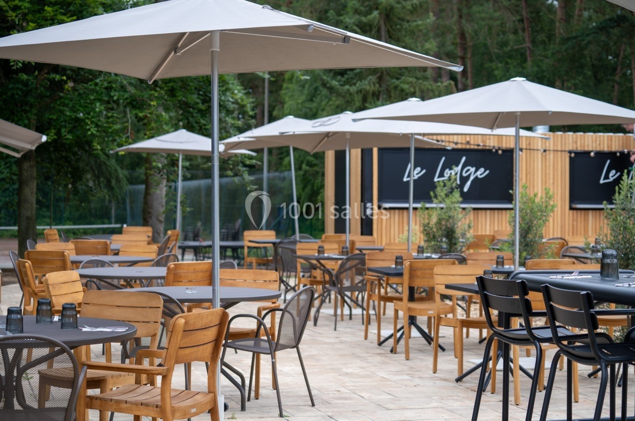 Terrasse extérieure avec tables et chaises en bois et métal, ombragée par des parasols, entourée de verdure.